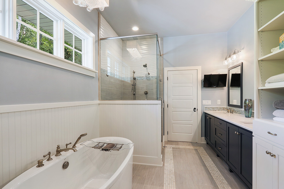 This is an example of a large beach style master bathroom in Other with shaker cabinets, black cabinets, a freestanding tub, a corner shower, gray tile, matchstick tile, grey walls, porcelain floors, an undermount sink, marble benchtops, beige floor and a hinged shower door.