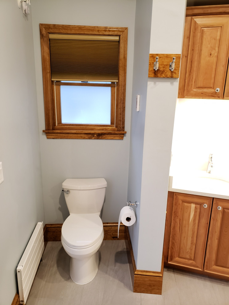 Photo of a mid-sized contemporary powder room in Boston with raised-panel cabinets, medium wood cabinets, a bidet, white tile, marble, blue walls, ceramic floors, an undermount sink, engineered quartz benchtops, grey floor, white benchtops, a built-in vanity and vaulted.