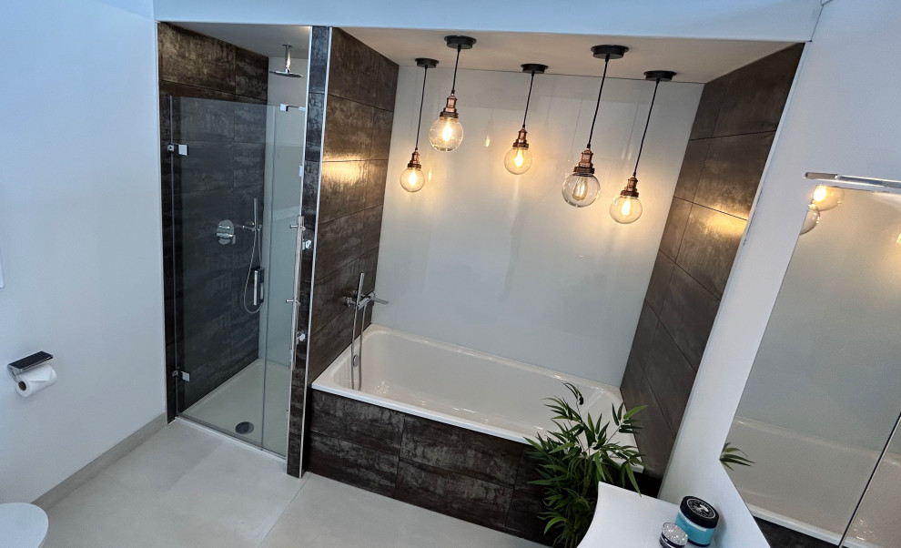 This is an example of a large eclectic master bathroom in Berkshire with flat-panel cabinets, a drop-in tub, an alcove shower, a wall-mount toilet, multi-coloured tile, porcelain tile, white walls, porcelain floors, an integrated sink, glass benchtops, grey floor, a hinged shower door, white benchtops, a single vanity and a floating vanity.