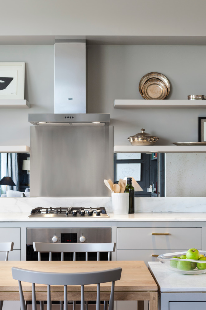 Inspiration for a contemporary open plan kitchen in London with flat-panel cabinets, grey cabinets, metallic splashback, mirror splashback, stainless steel appliances and with island.