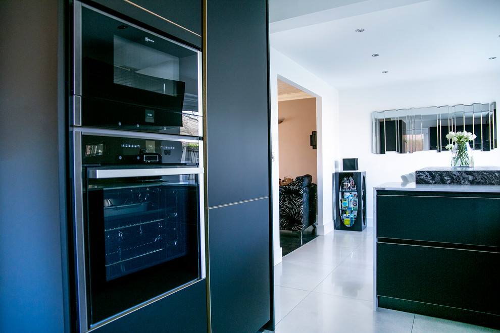 Mid-sized eclectic u-shaped eat-in kitchen in Manchester with an undermount sink, flat-panel cabinets, black cabinets, granite benchtops, orange splashback, glass sheet splashback, stainless steel appliances, porcelain floors, a peninsula, grey floor and multi-coloured benchtop.