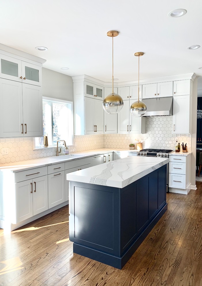 Example of a transitional l-shaped kitchen design with shaker cabinets, white cabinets, quartz countertops, white backsplash, an island and white countertops