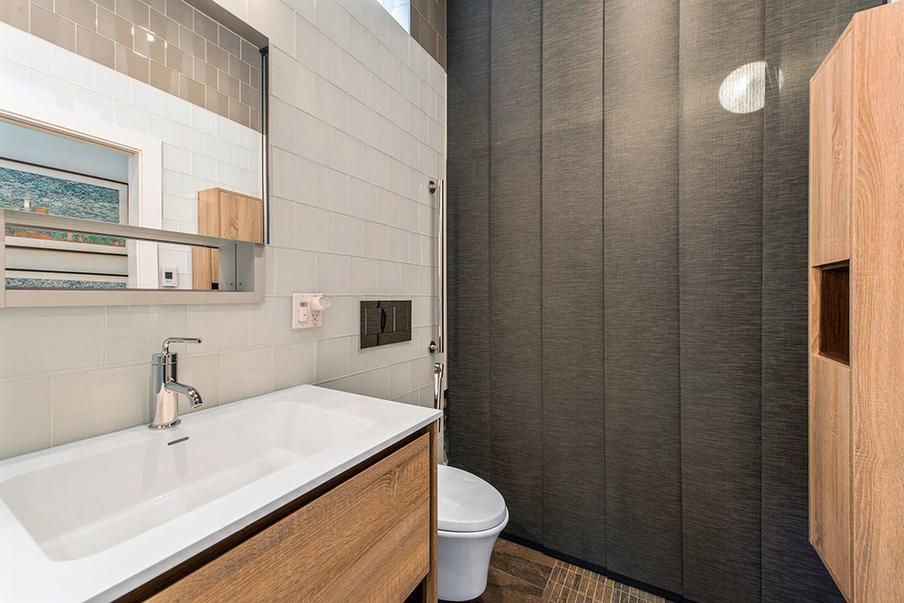 Photo of a small modern master bathroom in San Francisco with furniture-like cabinets, light wood cabinets, a drop-in tub, a wall-mount toilet, white tile, glass tile, white walls, ceramic floors, an integrated sink and laminate benchtops.