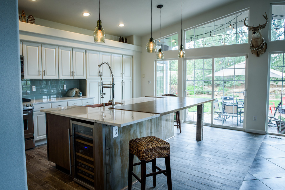 Large industrial l-shaped open plan kitchen in Denver with a farmhouse sink, raised-panel cabinets, white cabinets, quartz benchtops, blue splashback, glass tile splashback, stainless steel appliances, porcelain floors and with island.