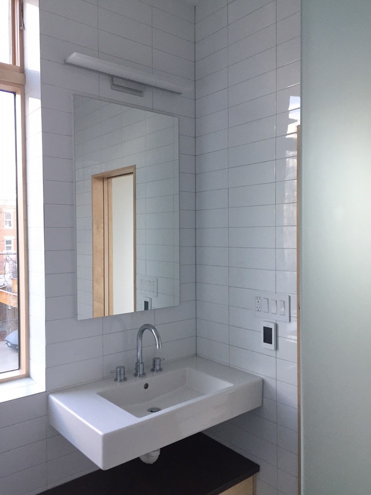 This is an example of a small industrial bathroom in DC Metro with a corner shower, a wall-mount toilet, blue tile, ceramic tile and white walls.