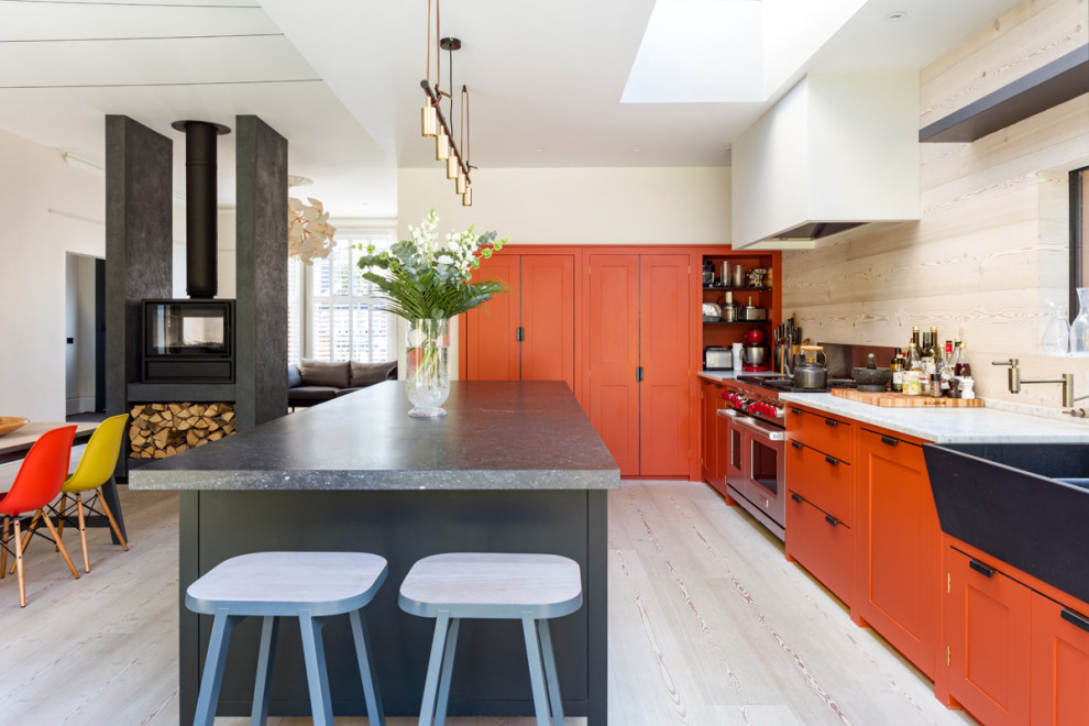 Large contemporary l-shaped eat-in kitchen in London with a farmhouse sink, shaker cabinets, orange cabinets, beige splashback, porcelain splashback, panelled appliances, porcelain floors, with island, beige floor and white benchtop.