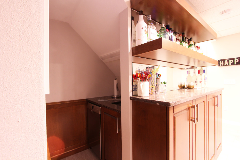 Photo of a small transitional u-shaped wet bar in Other with an undermount sink, raised-panel cabinets, medium wood cabinets, granite benchtops, vinyl floors, beige floor and mirror splashback.