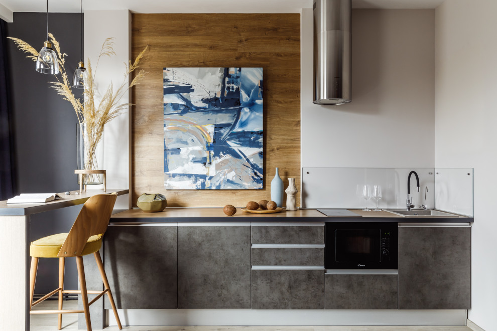 Photo of a small industrial l-shaped open plan kitchen in Other with an undermount sink, flat-panel cabinets, grey cabinets, wood benchtops, grey splashback, glass sheet splashback, panelled appliances, laminate floors, no island, beige floor and beige benchtop.