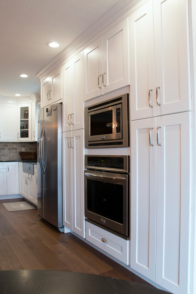 Inspiration for a large transitional l-shaped medium tone wood floor eat-in kitchen remodel with an undermount sink, shaker cabinets, white cabinets, granite countertops, stone tile backsplash, stainless steel appliances, an island and gray backsplash