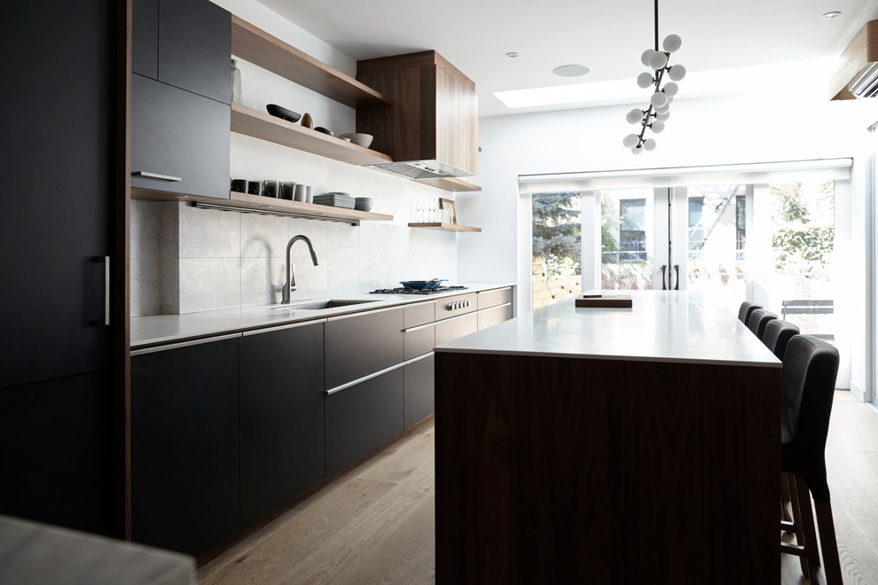 Design ideas for a mid-sized modern single-wall eat-in kitchen in New York with an undermount sink, flat-panel cabinets, black cabinets, quartzite benchtops, white splashback, travertine splashback, panelled appliances, light hardwood floors, with island and beige floor.