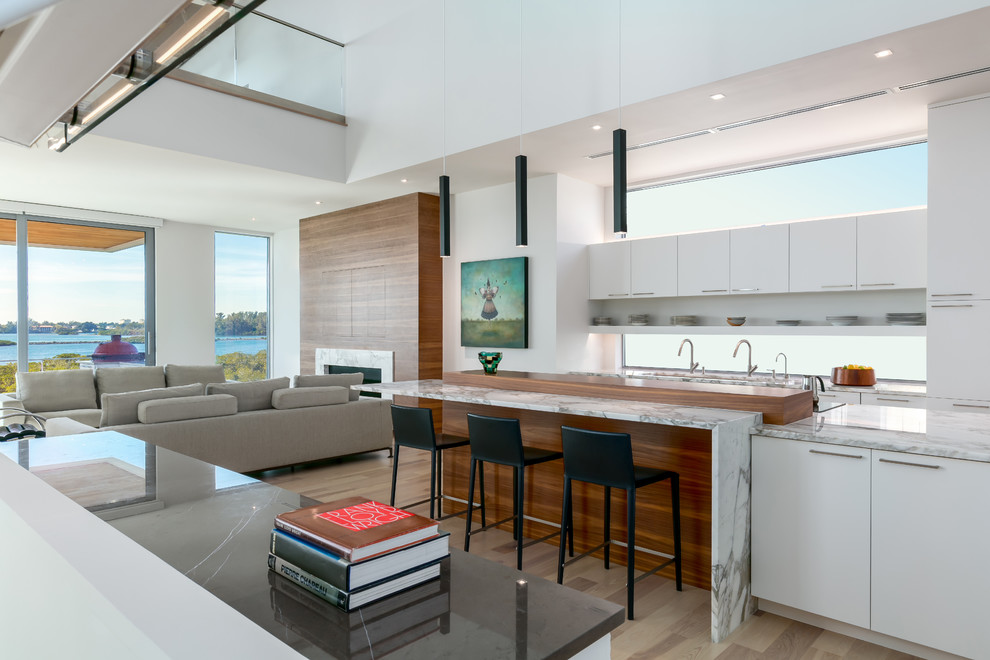 This is an example of a large contemporary single-wall open plan kitchen in Tampa with flat-panel cabinets, white cabinets, marble benchtops, window splashback, white appliances, medium hardwood floors, with island, brown floor and white benchtop.