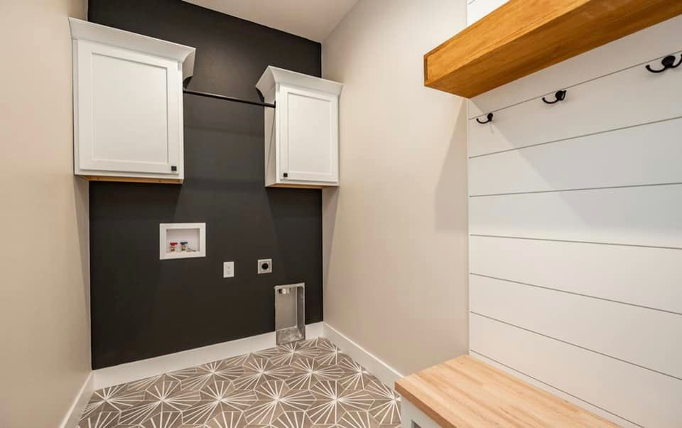 Photo of a small modern galley utility room in Cedar Rapids with white cabinets, white splashback, shiplap splashback, beige walls, ceramic floors, a side-by-side washer and dryer and beige floor.