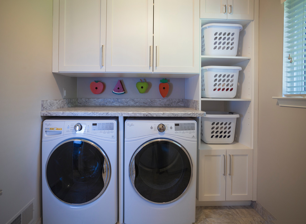 This is an example of a small contemporary galley dedicated laundry room in Detroit with a farmhouse sink, white cabinets, granite benchtops, beige walls, a side-by-side washer and dryer, beige floor, ceramic floors and shaker cabinets.