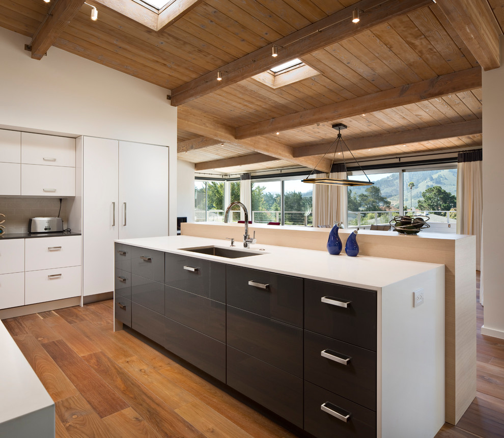 This is an example of a large contemporary l-shaped open plan kitchen in Other with an undermount sink, flat-panel cabinets, white cabinets, medium hardwood floors, quartz benchtops, panelled appliances, with island and brown floor.
