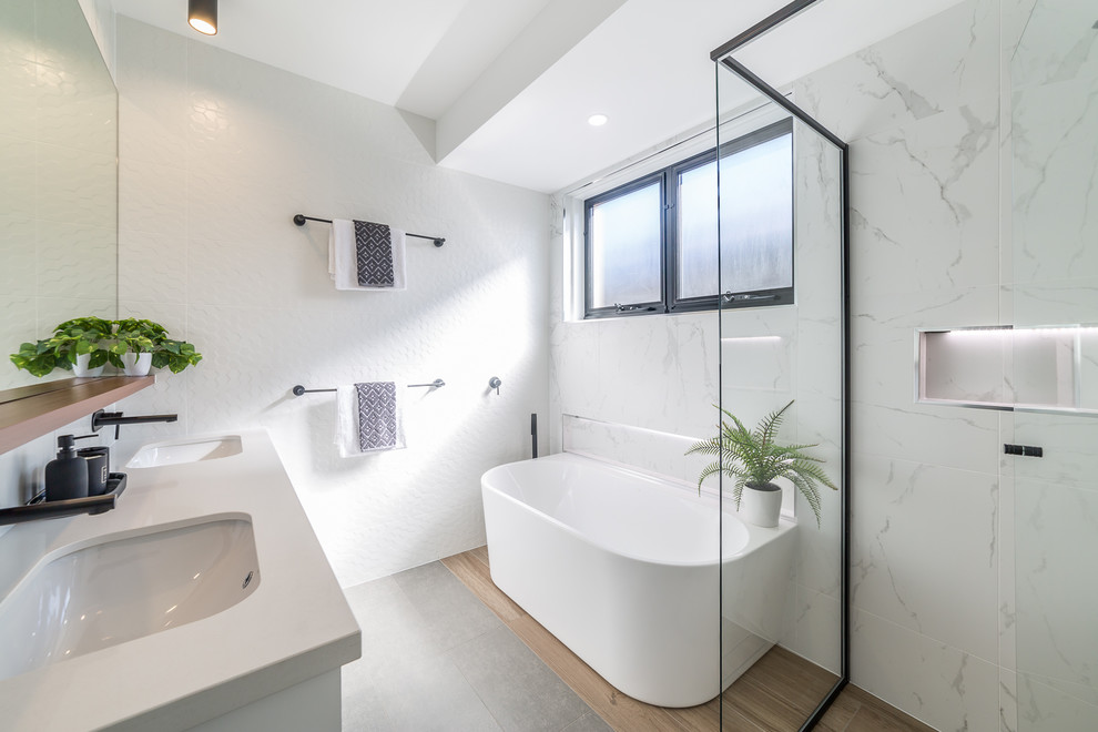Design ideas for a contemporary 3/4 bathroom in Brisbane with white cabinets, a freestanding tub, a corner shower, a two-piece toilet, white tile, ceramic tile, white walls, porcelain floors, an undermount sink, engineered quartz benchtops, grey floor, a hinged shower door and white benchtops.