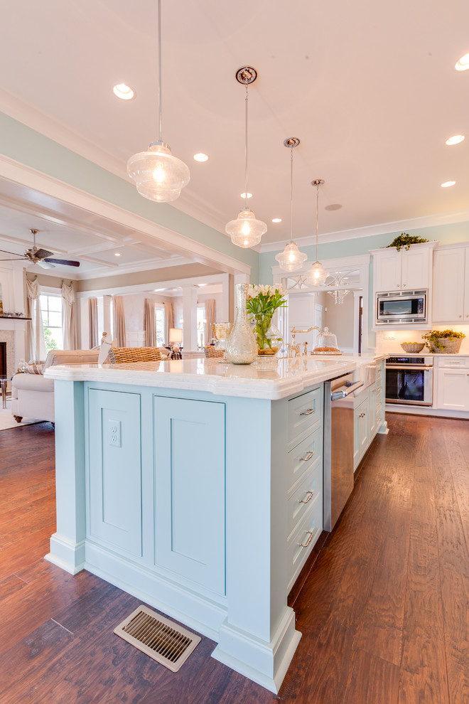 This is an example of a large beach style l-shaped open plan kitchen in Other with a farmhouse sink, recessed-panel cabinets, blue cabinets, marble benchtops, white splashback, stone tile splashback, stainless steel appliances, dark hardwood floors and with island.
