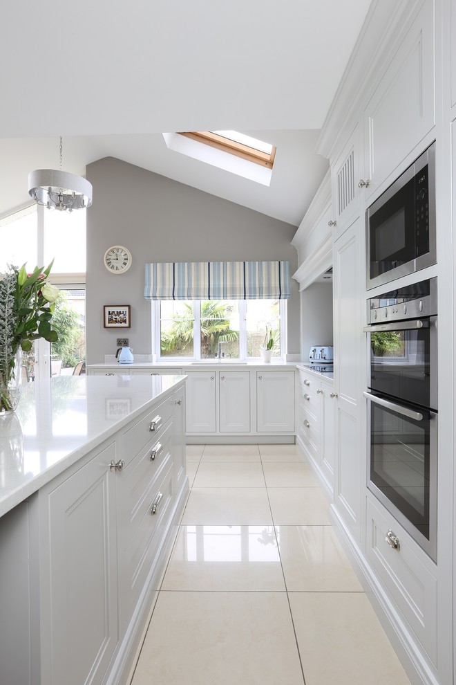Photo of a mid-sized transitional l-shaped eat-in kitchen in Dublin with an undermount sink, beaded inset cabinets, grey cabinets, quartz benchtops, white splashback, stone slab splashback, stainless steel appliances, porcelain floors and with island.