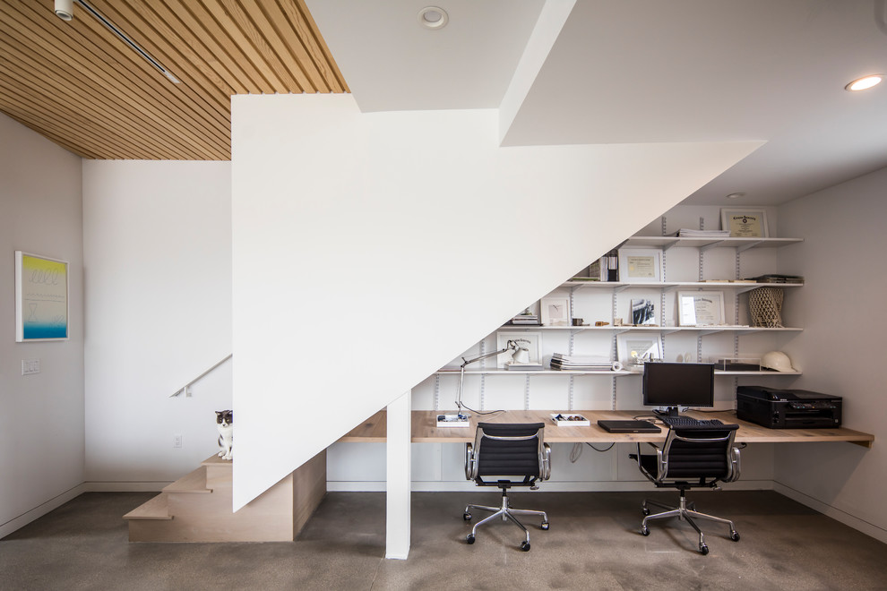 This is an example of a small modern study room in Los Angeles with white walls, concrete floors, a built-in desk and grey floor.