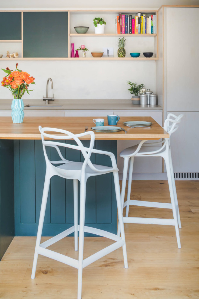 Photo of a medium sized contemporary l-shaped open plan kitchen in Oxfordshire with a built-in sink, flat-panel cabinets, engineered stone countertops, stainless steel appliances, medium hardwood flooring, an island, brown floors and beige worktops.