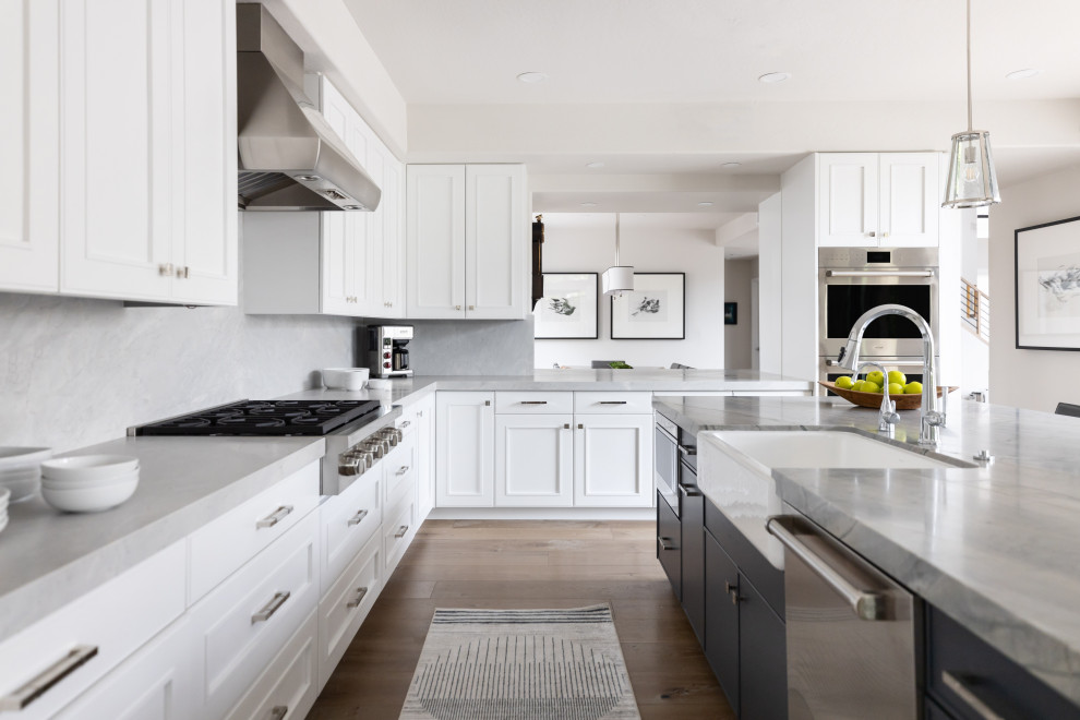 Inspiration for a large transitional medium tone wood floor and brown floor eat-in kitchen remodel in Phoenix with a farmhouse sink, recessed-panel cabinets, white cabinets, quartzite countertops, beige backsplash, stone slab backsplash, paneled appliances, an island and gray countertops