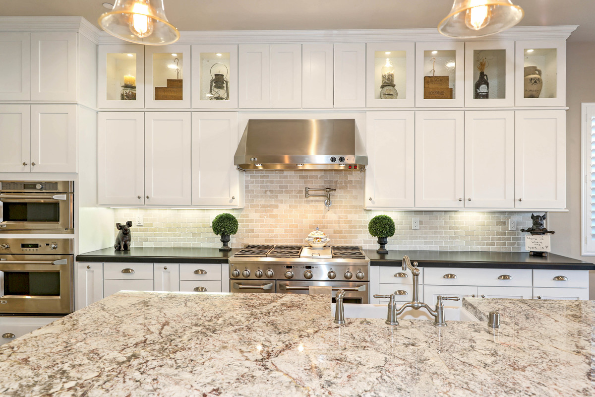 Inspiration for a large transitional l-shaped medium tone wood floor and brown floor open concept kitchen remodel in Orange County with a farmhouse sink, shaker cabinets, white cabinets, quartz countertops, beige backsplash, subway tile backsplash, stainless steel appliances and an island
