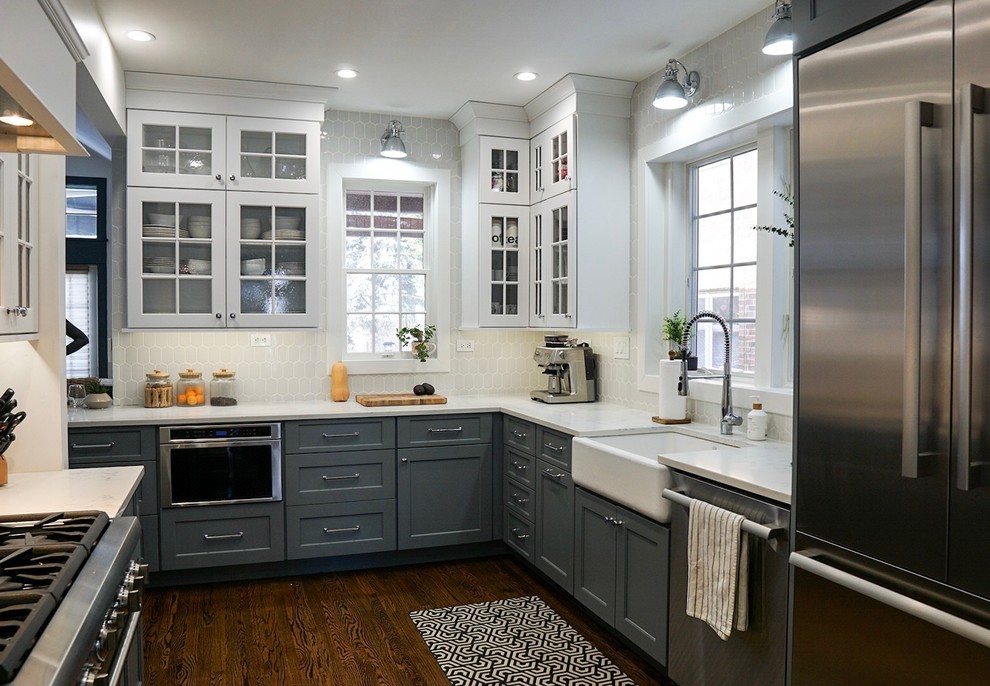 This is an example of a mid-sized traditional l-shaped eat-in kitchen in Chicago with a farmhouse sink, recessed-panel cabinets, white cabinets, quartz benchtops, white splashback, cement tile splashback, stainless steel appliances, dark hardwood floors, a peninsula, brown floor and white benchtop.
