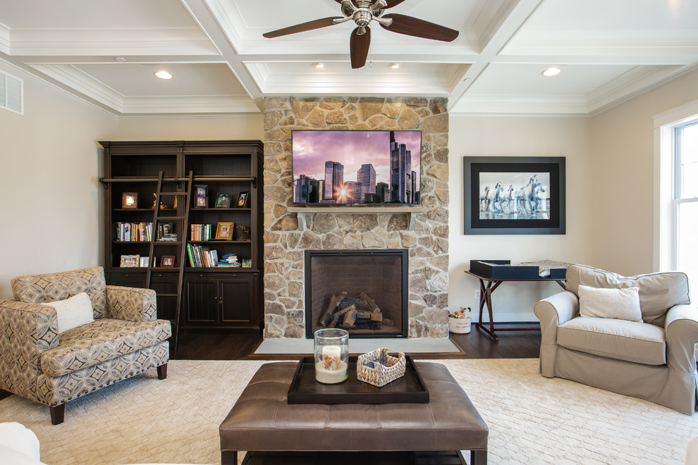 This is an example of a traditional living room in Baltimore with a library, beige walls, dark hardwood floors, a standard fireplace, a stone fireplace surround, a wall-mounted tv and brown floor.