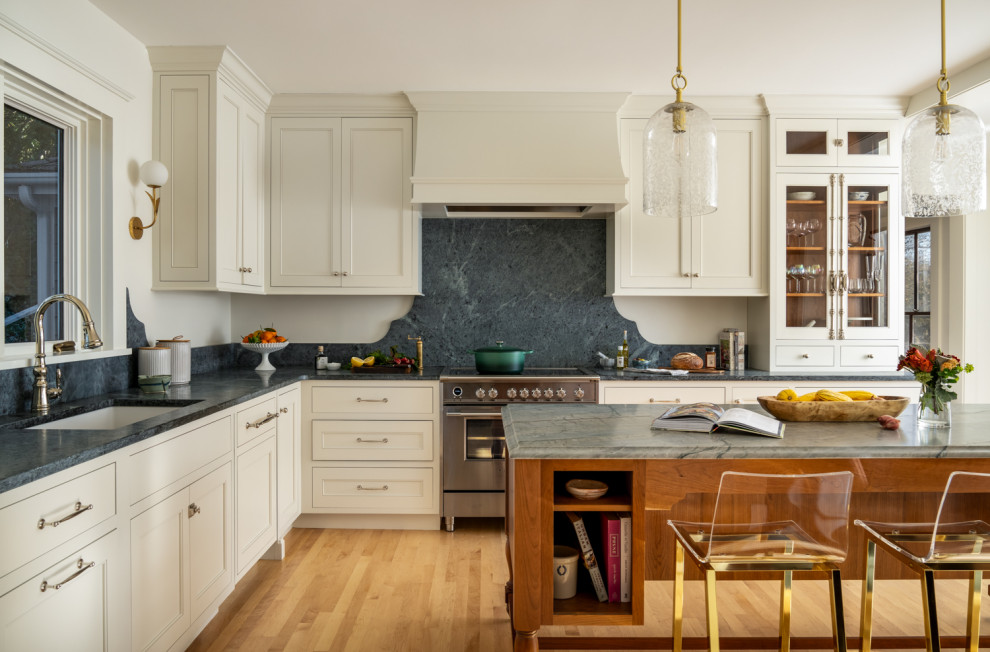 Example of a mid-sized classic l-shaped medium tone wood floor and brown floor kitchen design in Boston with an undermount sink, white cabinets, soapstone countertops, stone slab backsplash, stainless steel appliances, an island, recessed-panel cabinets, gray backsplash and gray countertops