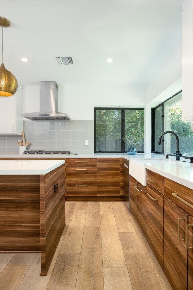 This is an example of a medium sized modern l-shaped open plan kitchen in Los Angeles with a belfast sink, flat-panel cabinets, medium wood cabinets, engineered stone countertops, grey splashback, metro tiled splashback, stainless steel appliances, laminate floors, an island, yellow floors and white worktops.