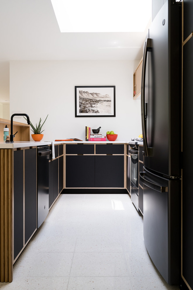 Design ideas for a mid-sized midcentury u-shaped eat-in kitchen in Indianapolis with an undermount sink, flat-panel cabinets, black cabinets, solid surface benchtops, white splashback, ceramic splashback, black appliances, terrazzo floors, no island, white floor and white benchtop.