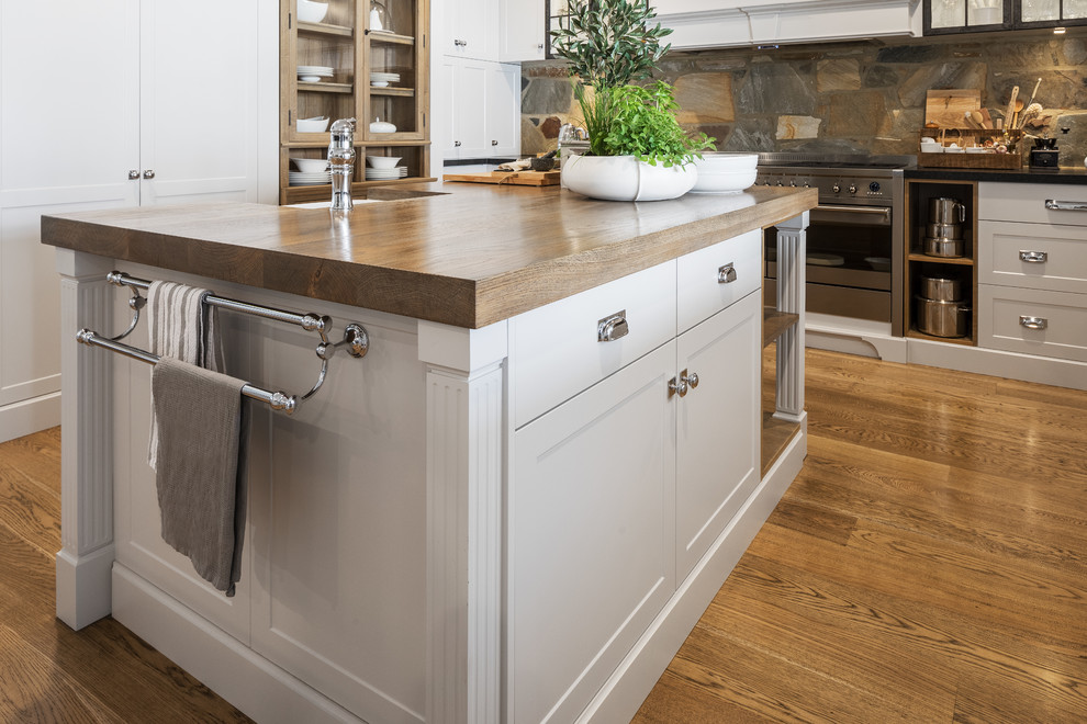 Large country kitchen in Perth with shaker cabinets, grey cabinets, brown splashback, stainless steel appliances, medium hardwood floors, with island, wood benchtops, a farmhouse sink, slate splashback and brown benchtop.