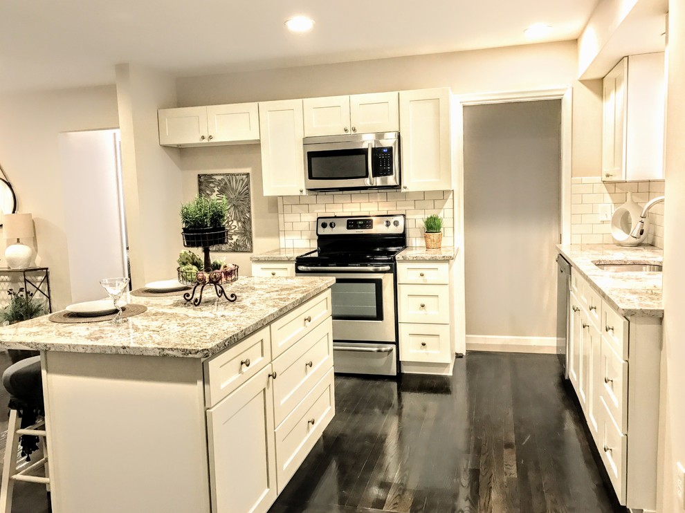 Inspiration for a mid-sized transitional l-shaped open plan kitchen in Detroit with an undermount sink, shaker cabinets, white cabinets, granite benchtops, white splashback, subway tile splashback, stainless steel appliances, dark hardwood floors, with island and brown floor.