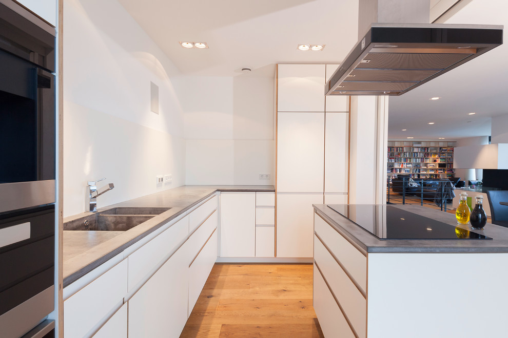 Design ideas for a large contemporary l-shaped open plan kitchen in Dortmund with a double-bowl sink, flat-panel cabinets, white cabinets, concrete benchtops, white splashback, panelled appliances, medium hardwood floors and with island.