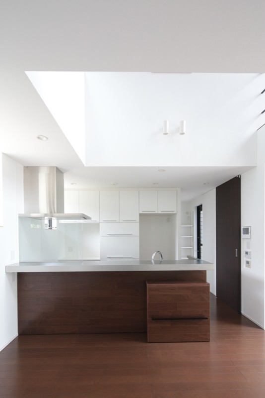 Photo of a modern galley kitchen in Tokyo with an integrated sink, flat-panel cabinets, white cabinets, stainless steel benchtops, white splashback, a peninsula and grey benchtop.