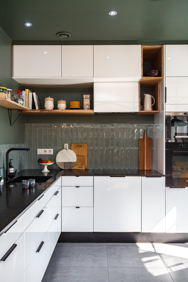 Idéer för att renovera ett avskilt, mellanstort skandinaviskt svart svart l-kök, med en undermonterad diskho, släta luckor, vita skåp, granitbänkskiva, grönt stänkskydd, stänkskydd i keramik, integrerade vitvaror, klinkergolv i keramik och grått golv