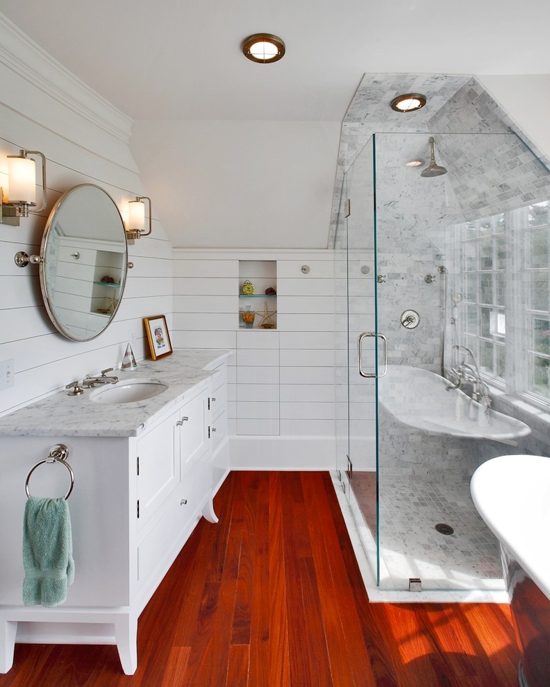 This is an example of a large beach style master bathroom in New York with an undermount sink, white cabinets, marble benchtops, a freestanding tub, a curbless shower, white tile, stone tile, white walls, dark hardwood floors, a hinged shower door and shaker cabinets.