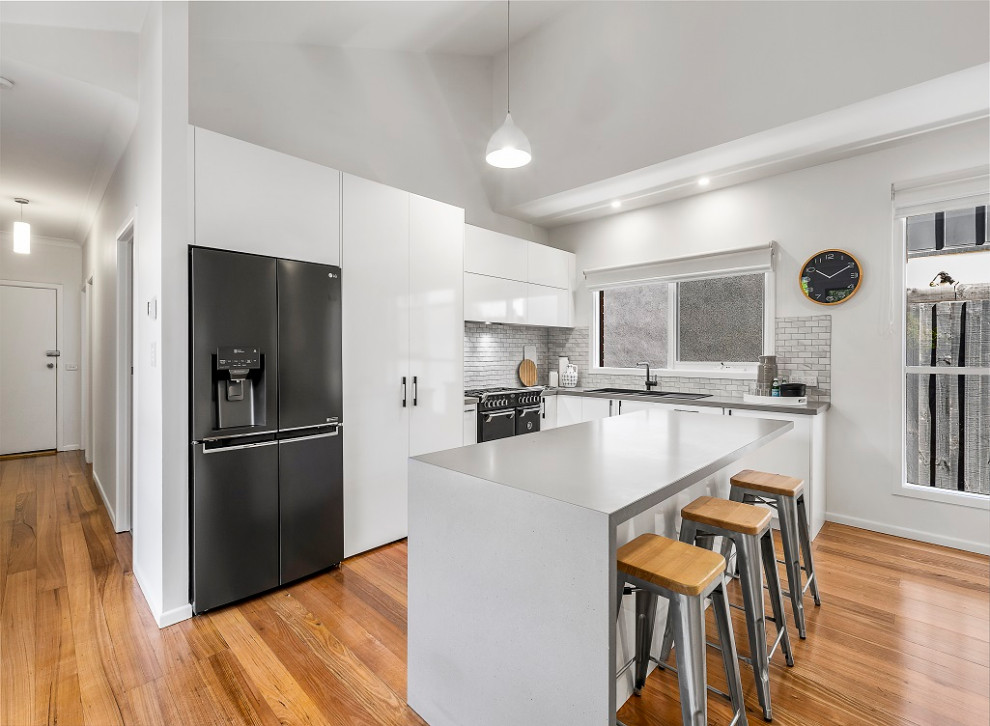 Eat-in kitchen - mid-sized contemporary l-shaped medium tone wood floor and brown floor eat-in kitchen idea in Melbourne with a double-bowl sink, flat-panel cabinets, white cabinets, quartz countertops, gray backsplash, ceramic backsplash, black appliances, an island and gray countertops