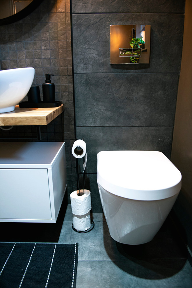 Cette image montre une salle de bain minimaliste de taille moyenne avec un placard en trompe-l'oeil, des portes de placard blanches, une douche ouverte, WC suspendus, un carrelage gris, mosaïque, un mur gris, un sol en carrelage de céramique, un plan vasque, un plan de toilette en bois, un sol noir, aucune cabine, un plan de toilette marron, meuble simple vasque et meuble-lavabo sur pied.