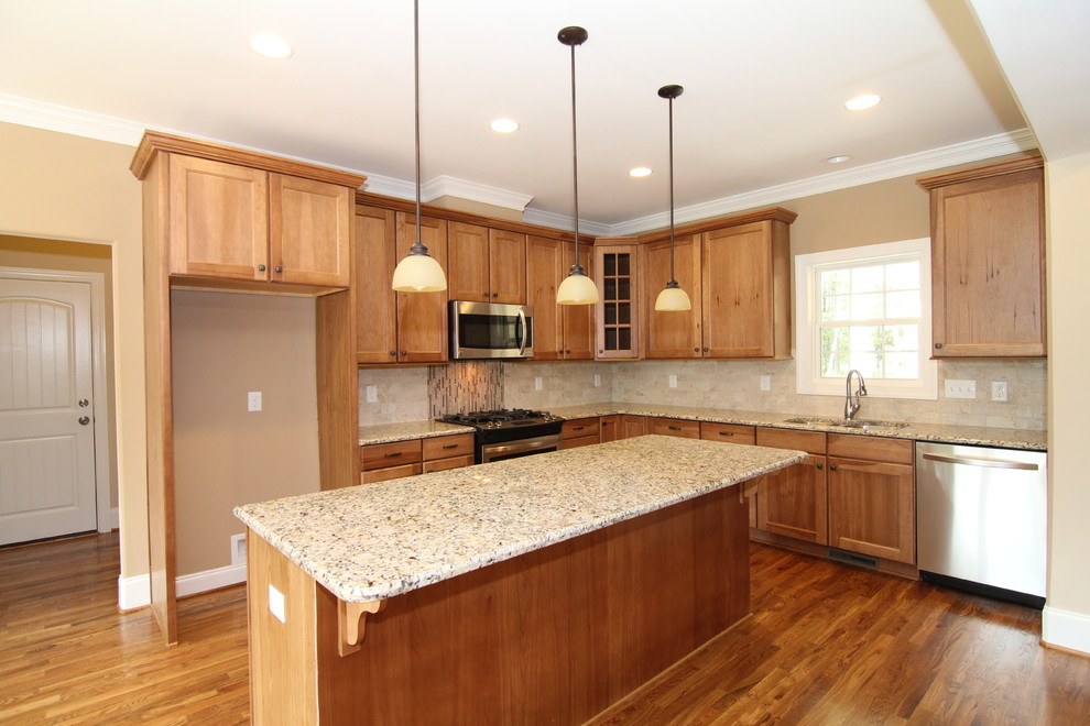 Photo of a mid-sized country l-shaped open plan kitchen in Raleigh with a double-bowl sink, recessed-panel cabinets, light wood cabinets, granite benchtops, beige splashback, ceramic splashback, stainless steel appliances, light hardwood floors and with island.