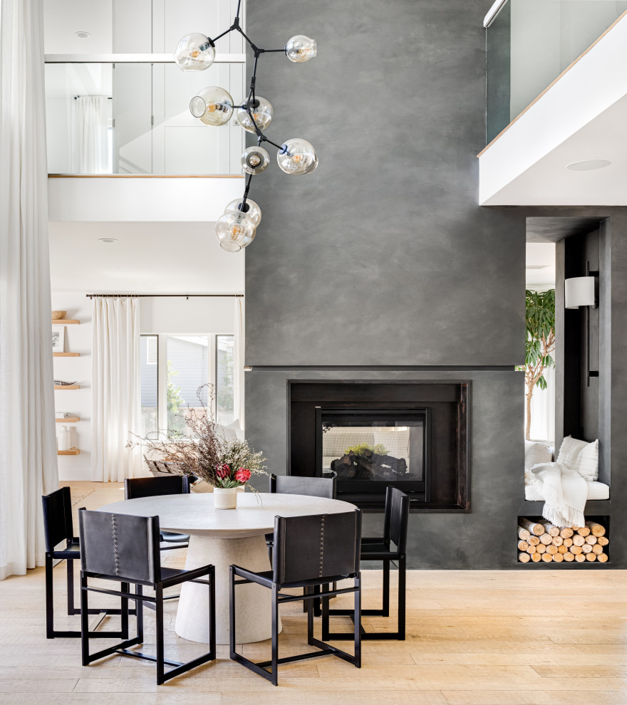 Inspiration for a scandinavian open plan dining in San Diego with white walls, light hardwood floors, a two-sided fireplace, a plaster fireplace surround and beige floor.