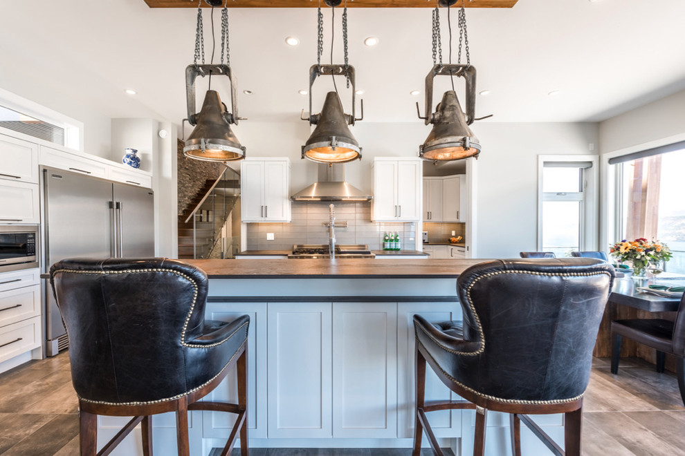 This is an example of a large industrial galley eat-in kitchen in Vancouver with an undermount sink, shaker cabinets, white cabinets, solid surface benchtops, grey splashback, glass tile splashback, stainless steel appliances, porcelain floors, with island and brown floor.