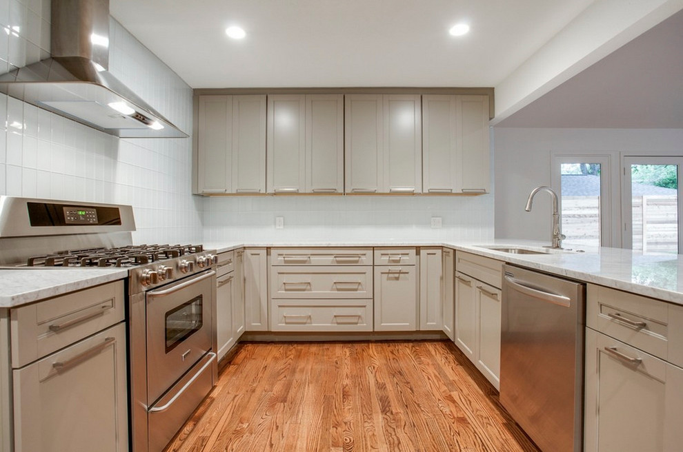 Small transitional u-shaped medium tone wood floor kitchen photo with a single-bowl sink, recessed-panel cabinets, gray cabinets, marble countertops, white backsplash, glass tile backsplash and stainless steel appliances