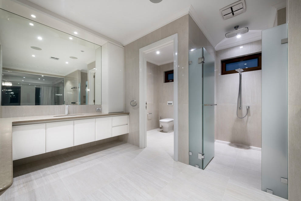 This is an example of an expansive contemporary master bathroom in Perth with white cabinets, an undermount tub, an alcove shower, a two-piece toilet, beige tile, porcelain tile, beige walls, porcelain floors, an undermount sink, engineered quartz benchtops, beige floor and a hinged shower door.