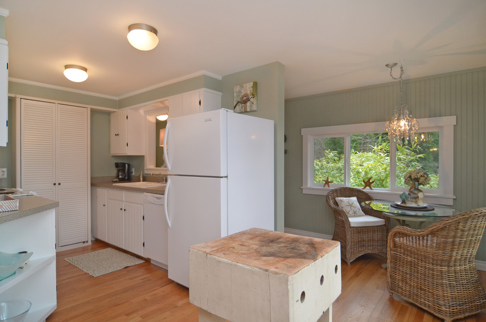 This is an example of a small beach style galley eat-in kitchen in Seattle with a double-bowl sink, beaded inset cabinets, white cabinets, laminate benchtops, white appliances and light hardwood floors.
