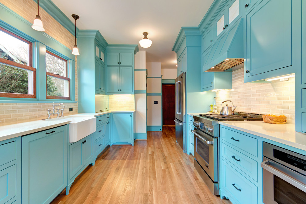 Photo of a large traditional galley separate kitchen in Portland with a farmhouse sink, shaker cabinets, blue cabinets, quartz benchtops, beige splashback, subway tile splashback, stainless steel appliances, light hardwood floors and no island.