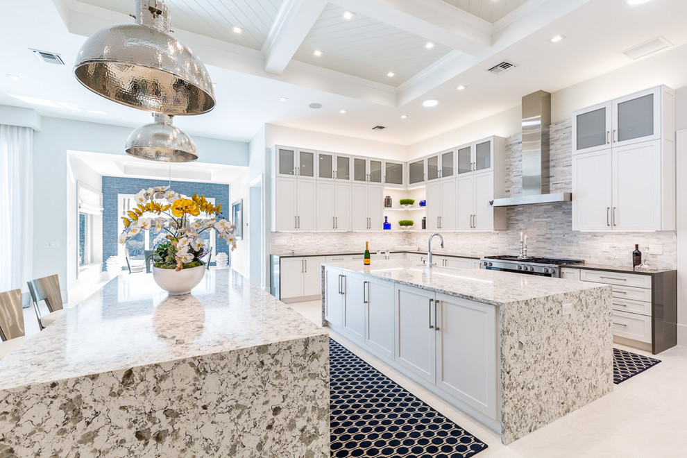 This is an example of a large transitional l-shaped open plan kitchen in Miami with a farmhouse sink, recessed-panel cabinets, white cabinets, granite benchtops, grey splashback, matchstick tile splashback, stainless steel appliances, porcelain floors, multiple islands and white floor.