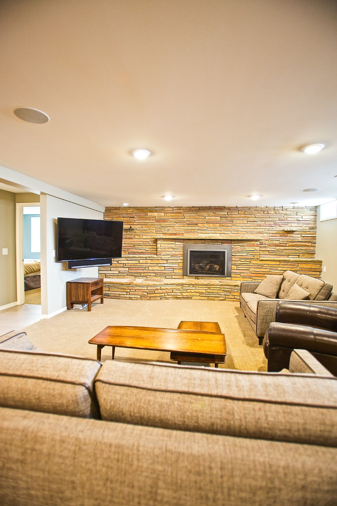 Photo of a midcentury basement in Minneapolis with carpet, a standard fireplace, a stone fireplace surround and beige floor.