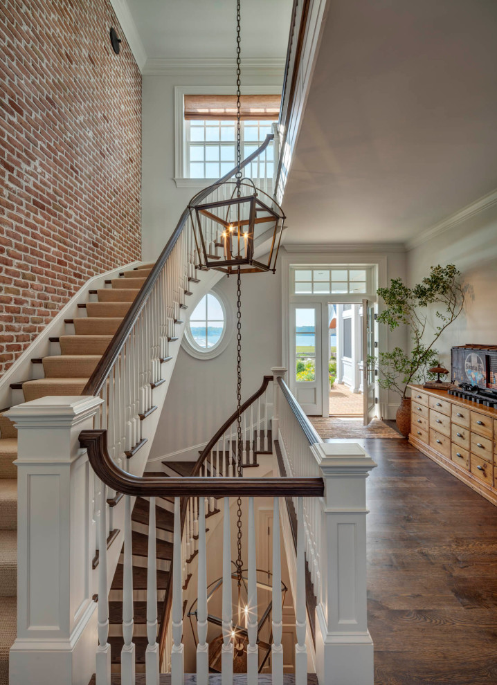 Стильный дизайн: большая изогнутая лестница в классическом стиле с ступенями с ковровым покрытием, ковровыми подступенками, деревянными перилами и кирпичными стенами - последний тренд