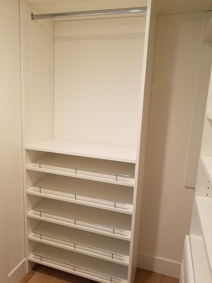 This is an example of a small beach style gender-neutral walk-in wardrobe in Orange County with flat-panel cabinets, white cabinets, light hardwood floors and beige floor.