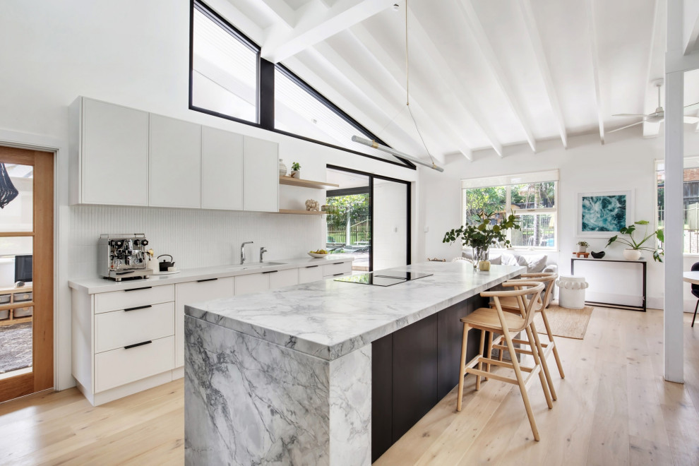 Photo of a mid-sized transitional l-shaped open plan kitchen in Sydney with an undermount sink, flat-panel cabinets, dark wood cabinets, granite benchtops, white splashback, matchstick tile splashback, black appliances, light hardwood floors, with island, beige floor, grey benchtop, exposed beam and vaulted.